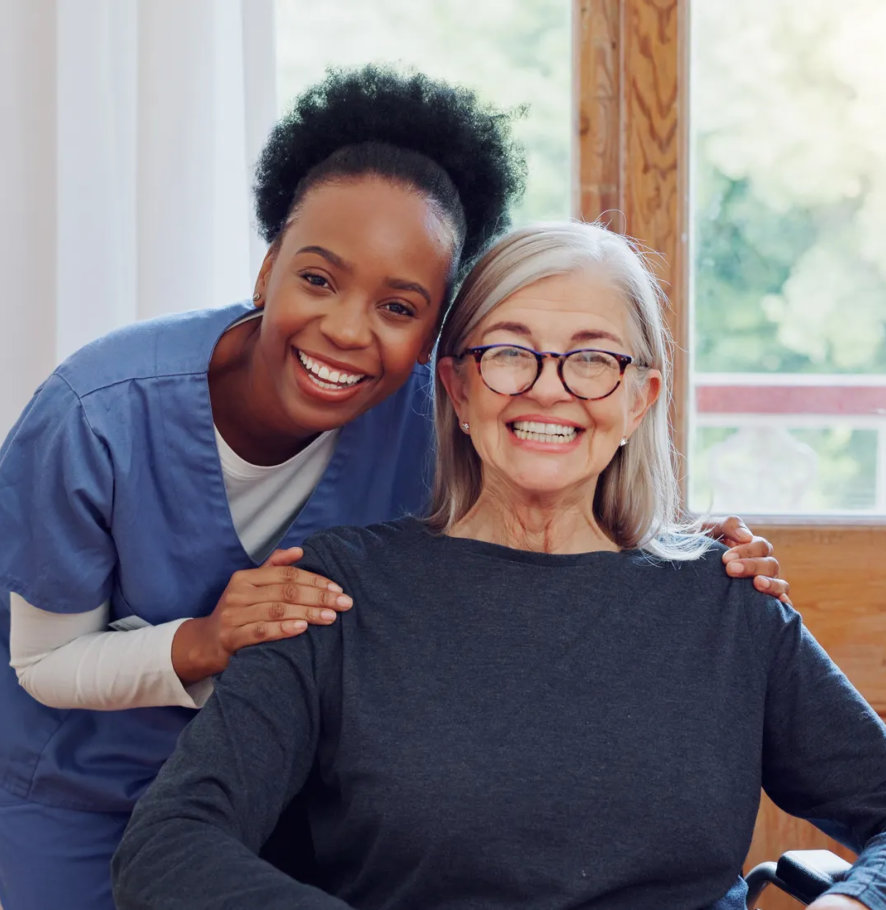 A caregiver hugging a smiling woman in a wheelchair by a window