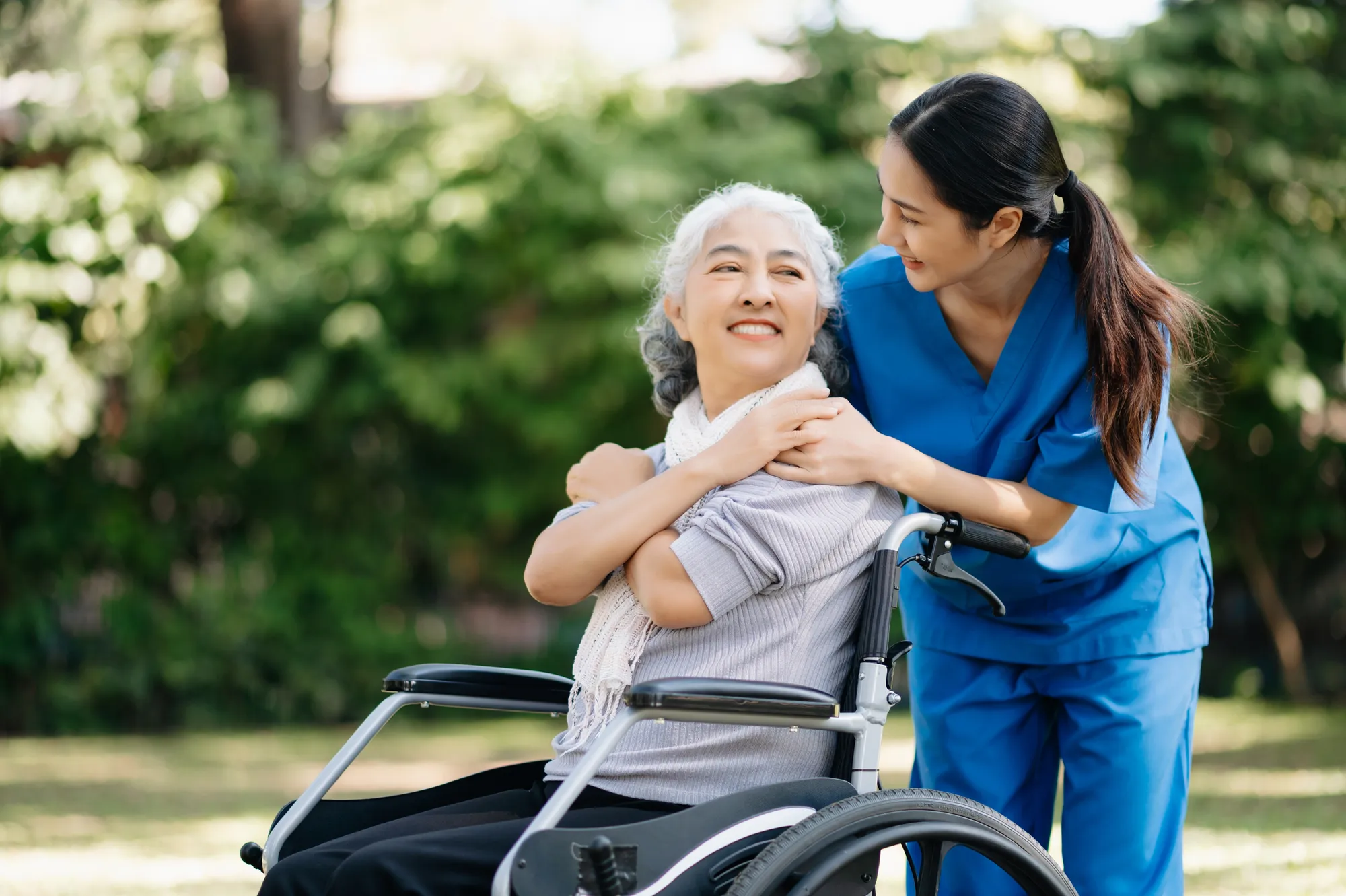 a caregiver embracing a smiling woman in a wheelchair outdoors